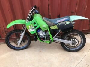 Green Kawasaki KX250 dirt bike beside a shipping container